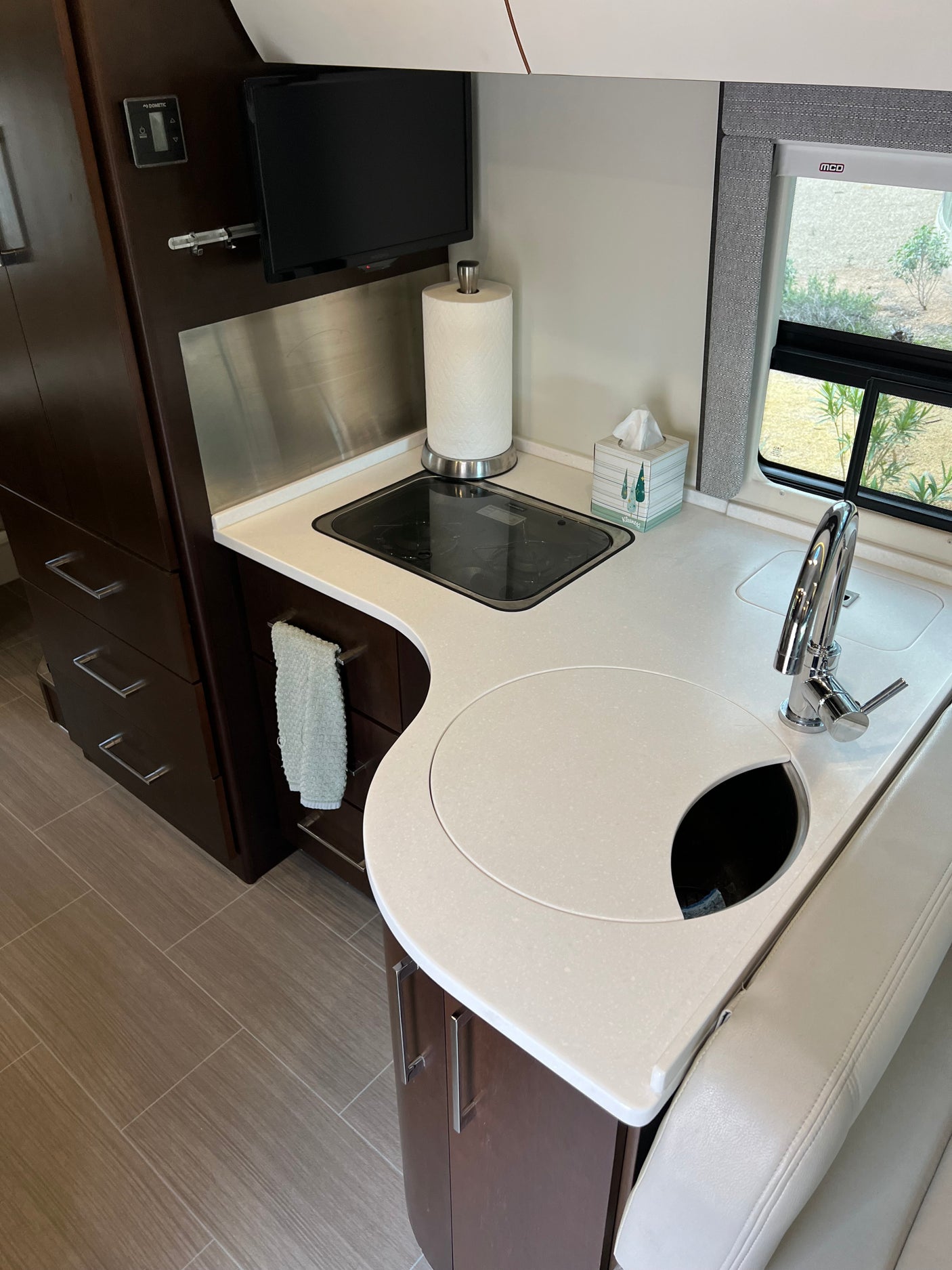 Inside a sleek **RV rental**. This compact kitchen features a modern countertop, sink, stovetop, and dark wood cabinetry.