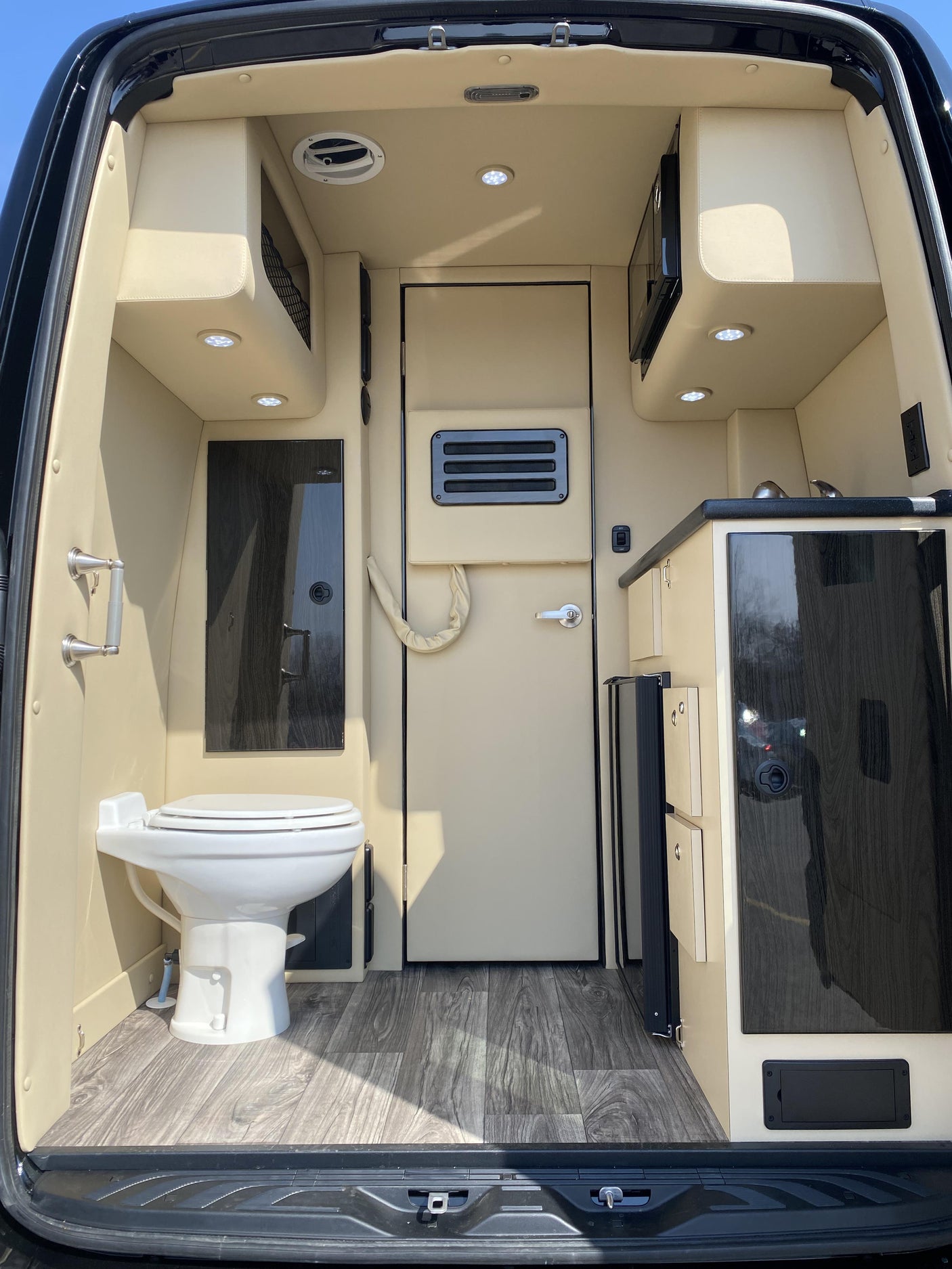 Inside a luxurious RV rental, featuring a compact kitchen, bathroom with toilet, and elegant wood flooring.