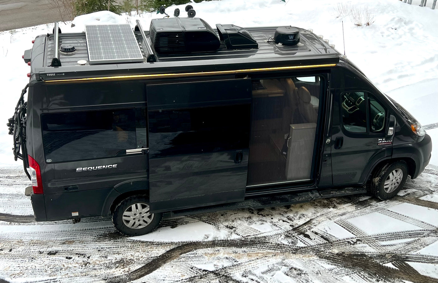 Sleek dark gray RV rental camper van, equipped for adventures with solar panels, AC, and a bike rack.