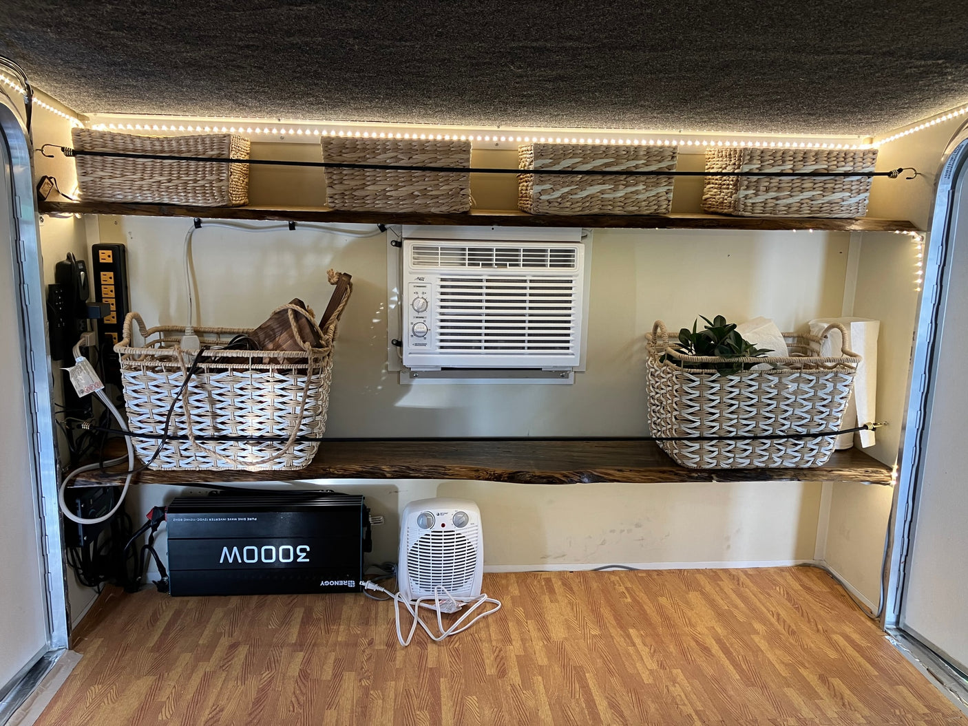 Cozy RV rental interior with organized storage, AC, and lighting, featuring wood shelves, wicker baskets, and a power setup.