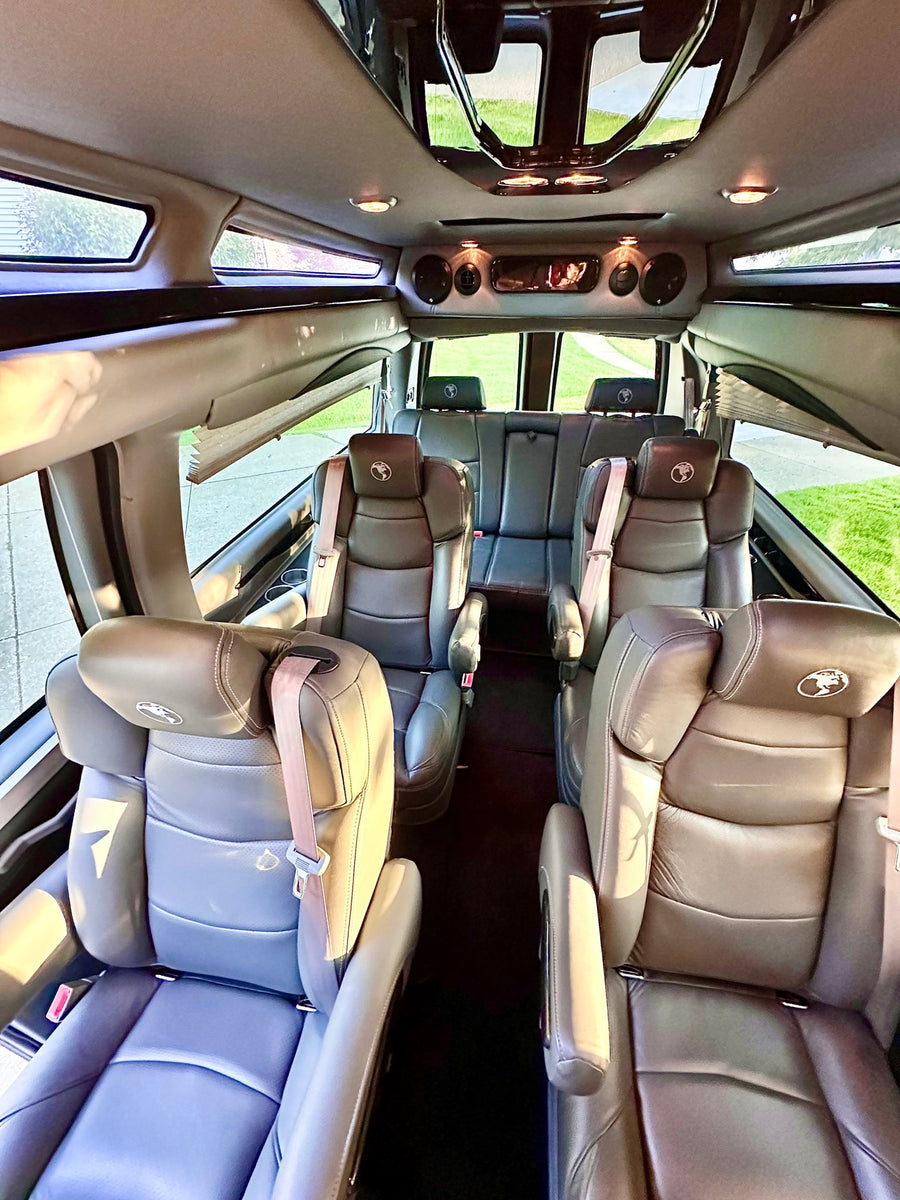 parked on a driveway next to a brick house and tree.|Experience comfort in this RV rental! Interior view of a spacious van