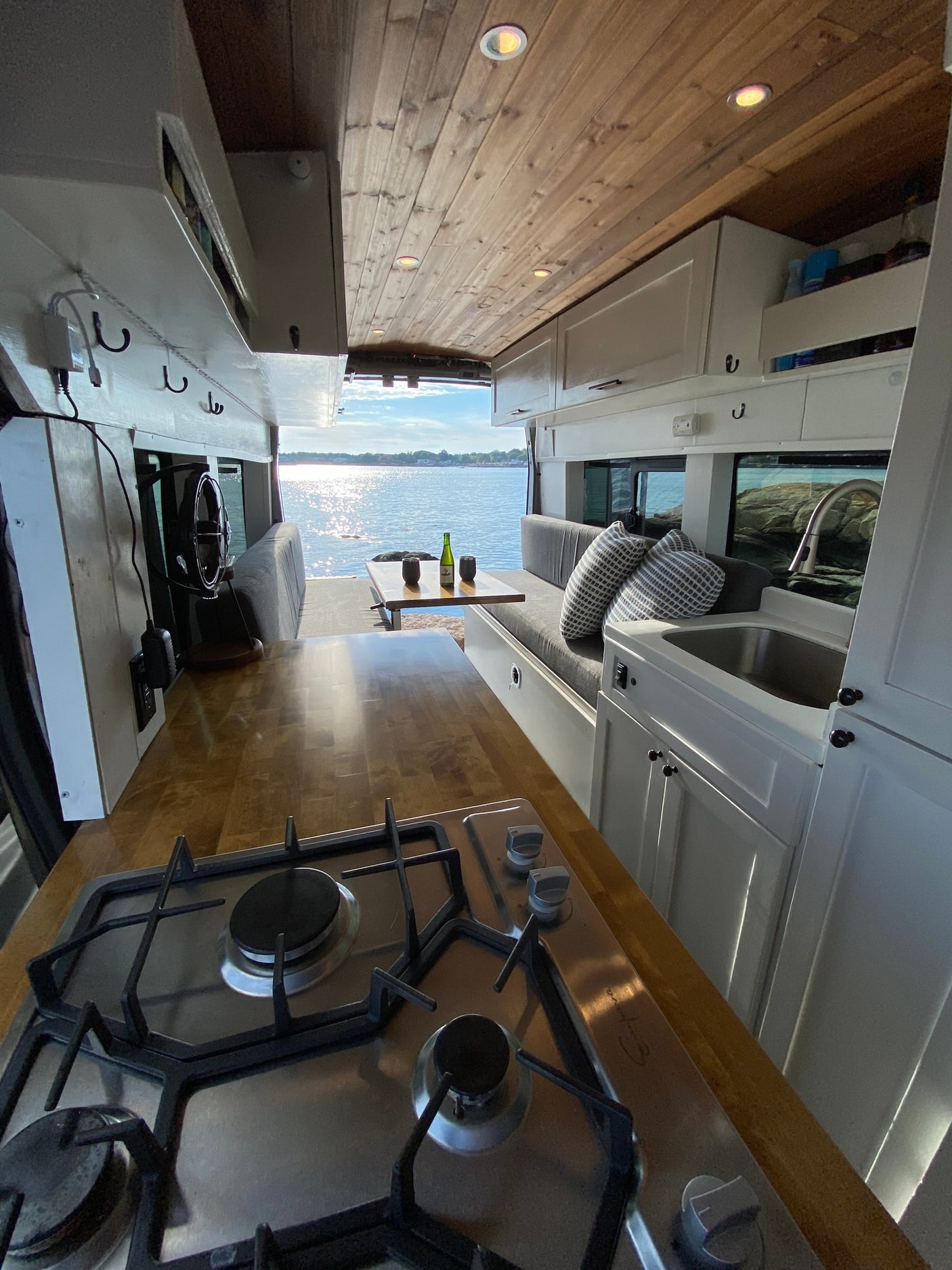 enjoying the vibrant view over water from inside the camper van.|Enjoy a breathtaking sunset from this RV rental van parked by the water. The golden sky and sea are mirrored on its reflective side