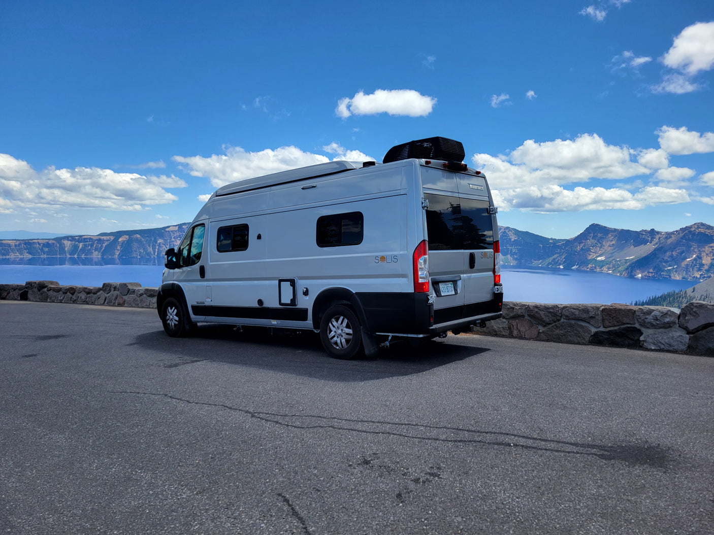 This RV rental, a Winnebago Solis, offers breathtaking views of Crater Lake's deep blue water and surrounding mountains.