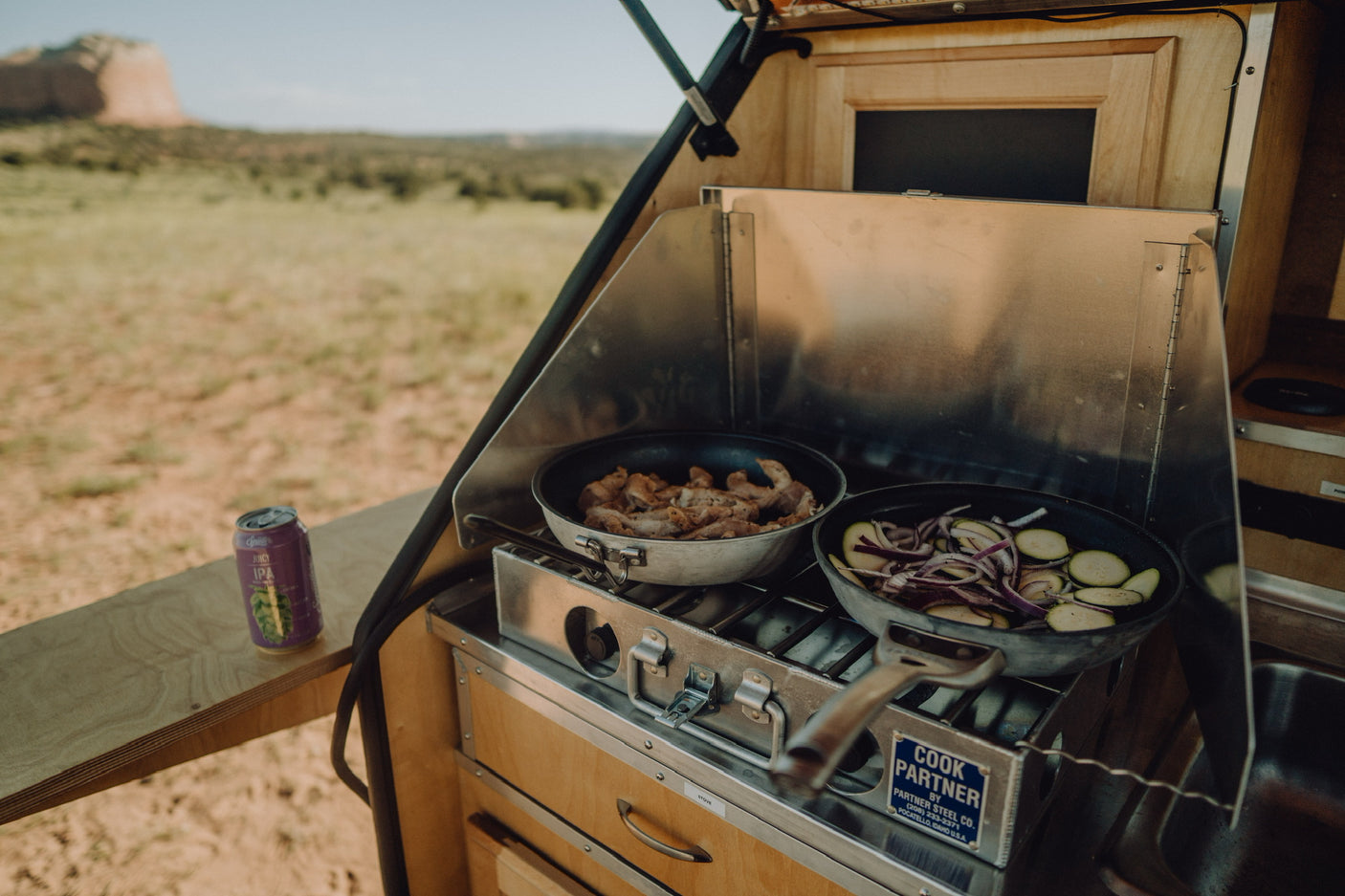Enjoying an RV rental outdoor kitchen, preparing a camp meal with meat & veggies on the stove, cold beer ready. Adventure awaits!