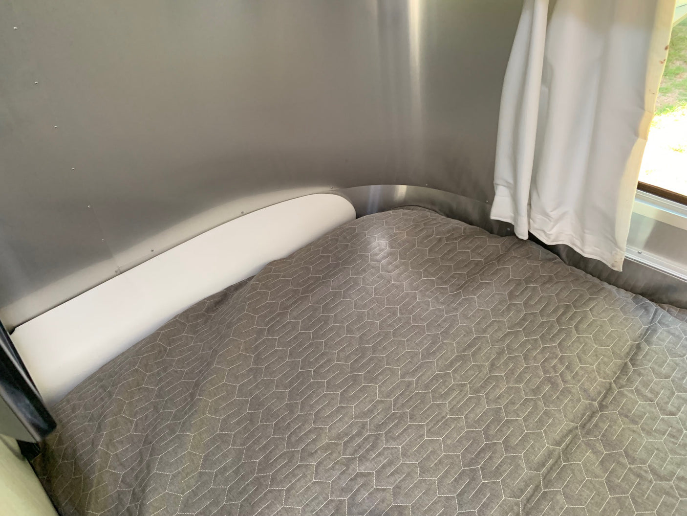 is parked on a gravel lot under a clear sky.|Cozy RV rental sleeping area features quilted grey bedding