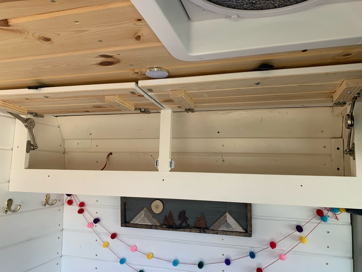 Inside an RV rental: open overhead wooden cabinets reveal storage. Custom wood-paneled ceiling & walls with playful decor.