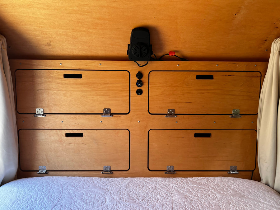 Cozy wooden interior of an RV rental, showing built-in storage, fan, & charging ports above a bed.