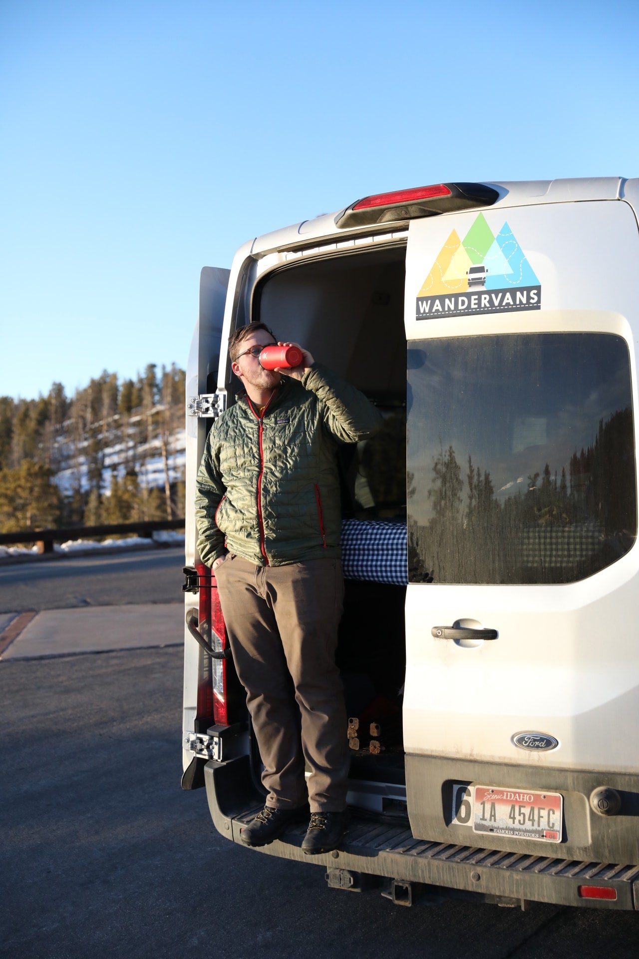 Man relaxing in a Wandervans RV rental. He lies in the Ford van's back with feet out, drinking from a red cup.