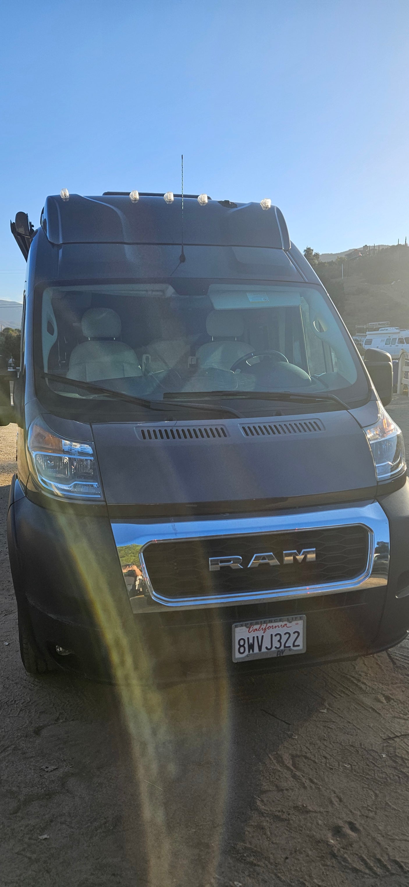 Front of a dark grey Ram ProMaster camper van, an RV rental, parked on dirt. CA license 8WVJ322 visible.