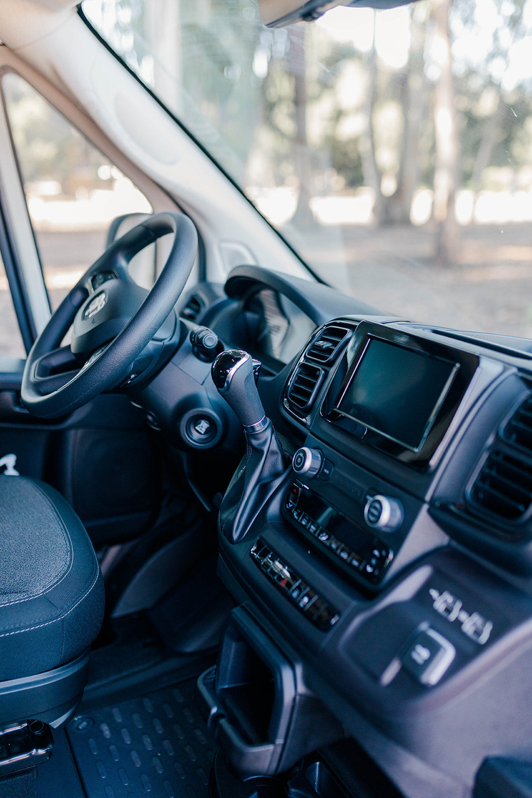 Inside a modern RV rental: The driver's area with steering wheel, dashboard, infotainment screen, and gear shift.