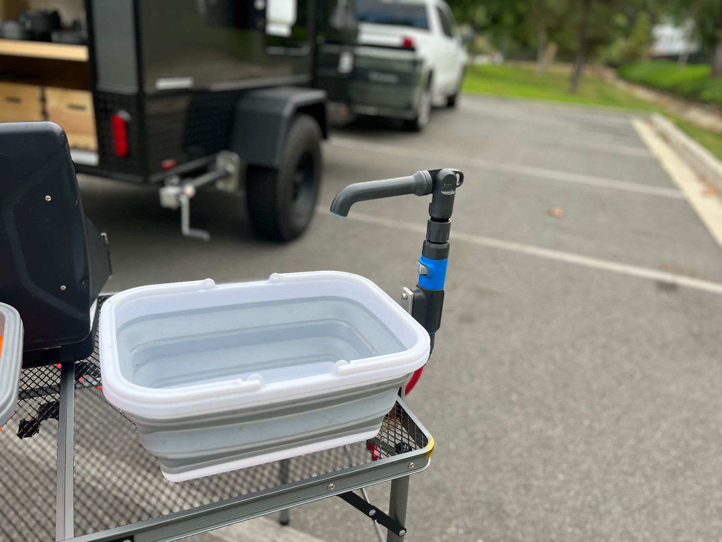 RV rental outdoor kitchen: Portable wash basin with faucet on a table, ready for use beside a camper trailer.