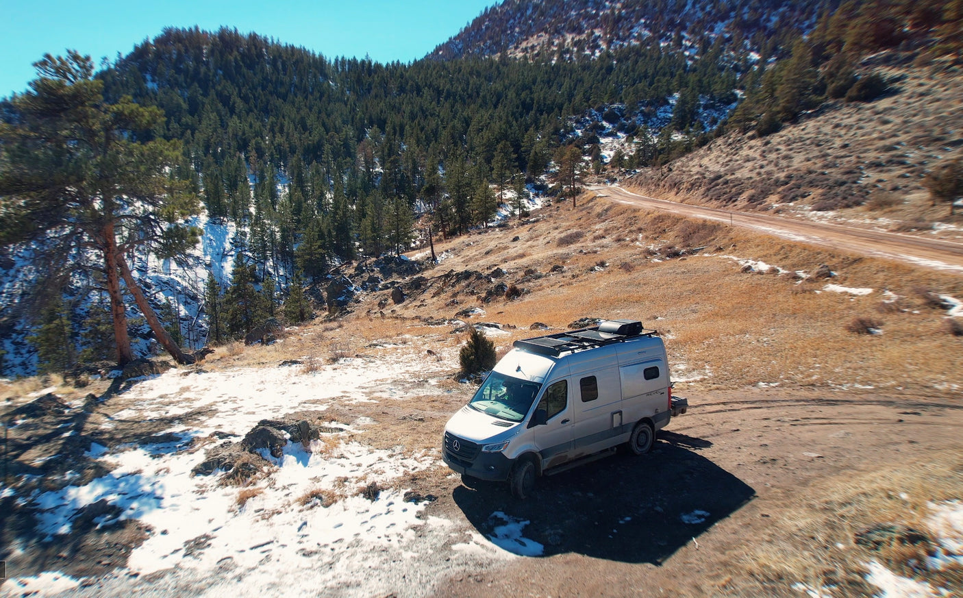 Light gray RV rental van parked on a snowy mountain dirt road, ideal for winter adventures.
