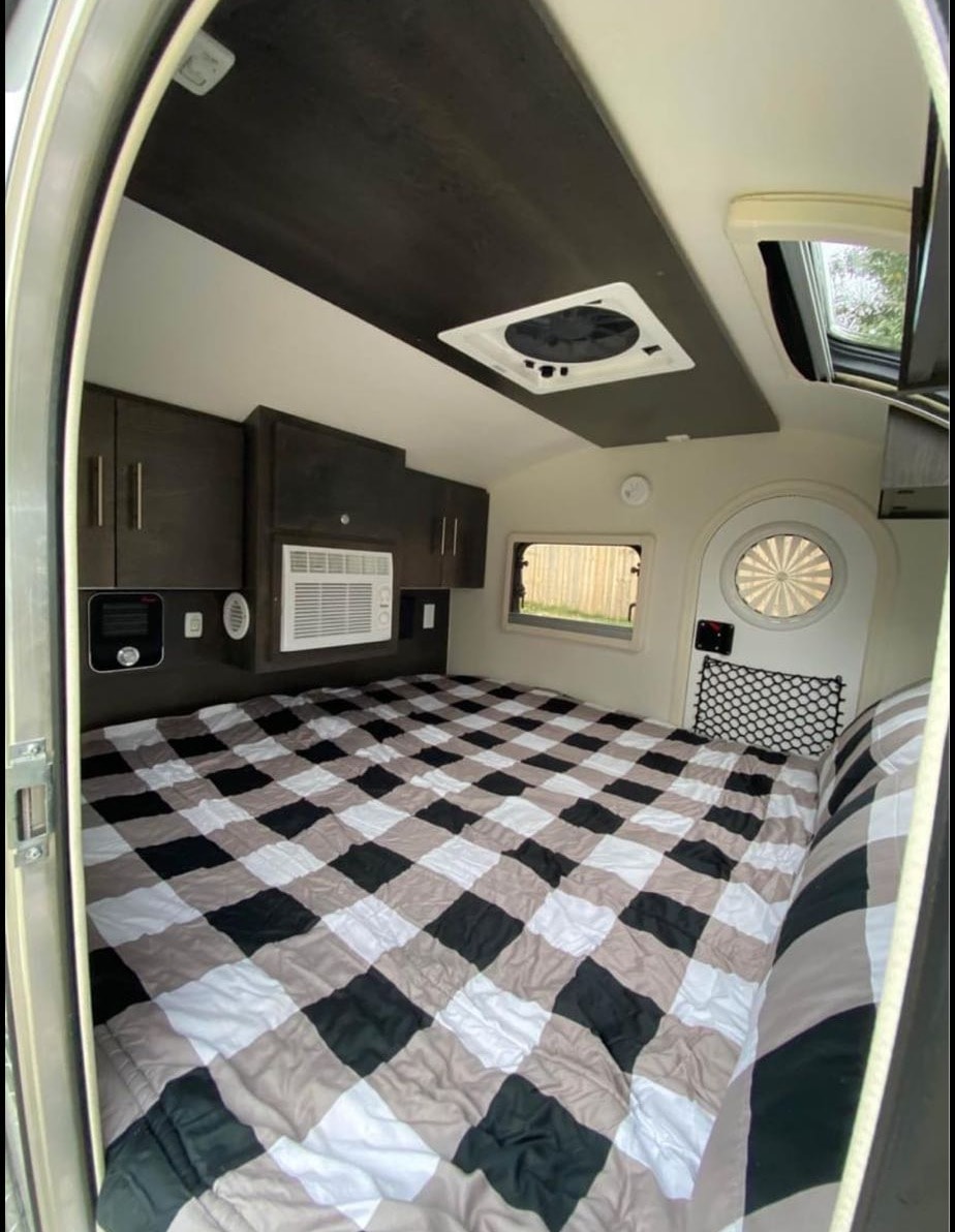 This RV rental's sleeping area features a large checkered bed, AC, overhead storage & vent.