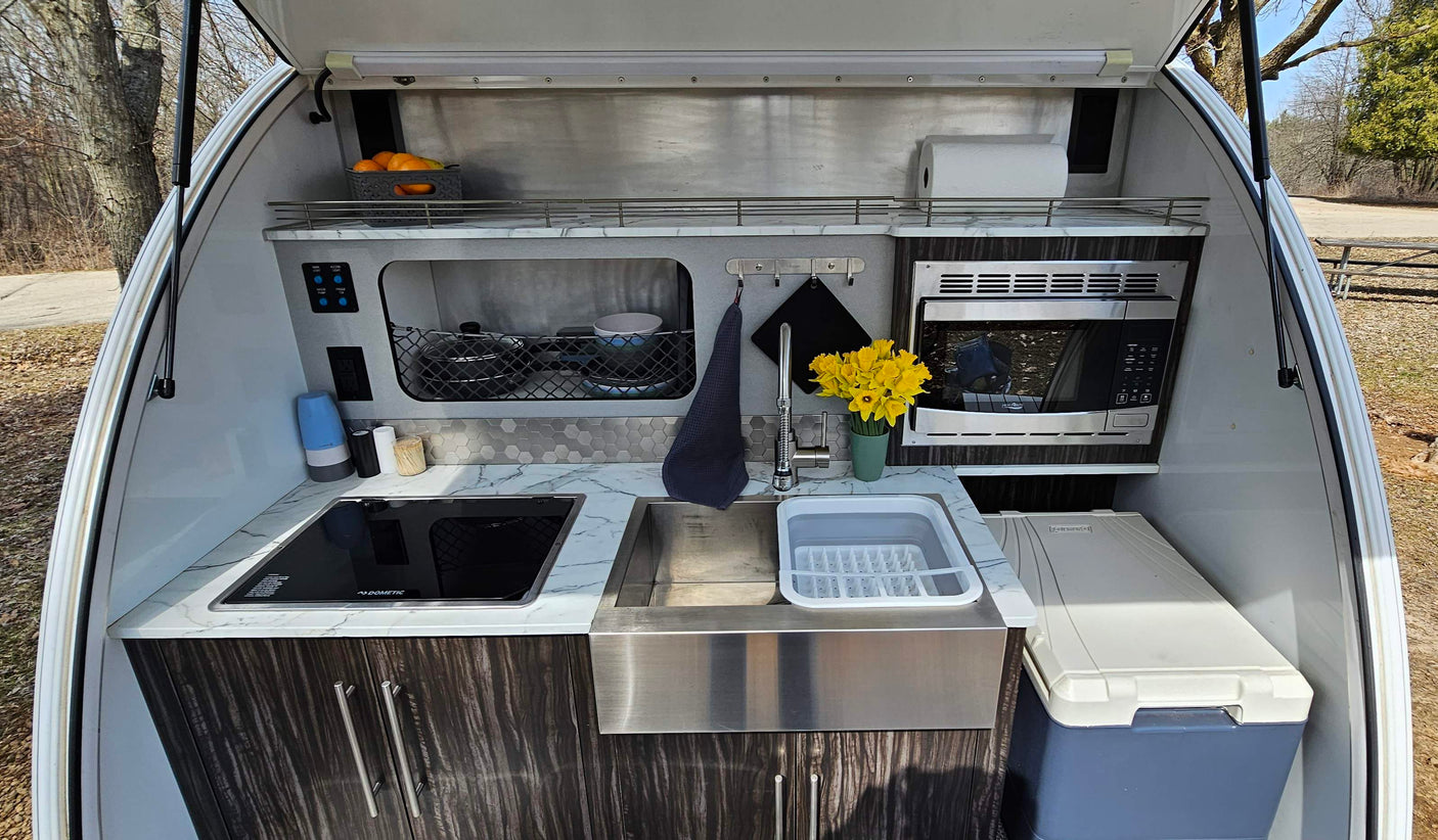 Compact outdoor RV rental kitchen with Dometic stovetop, sink, microwave, and cooler for convenient camping.
