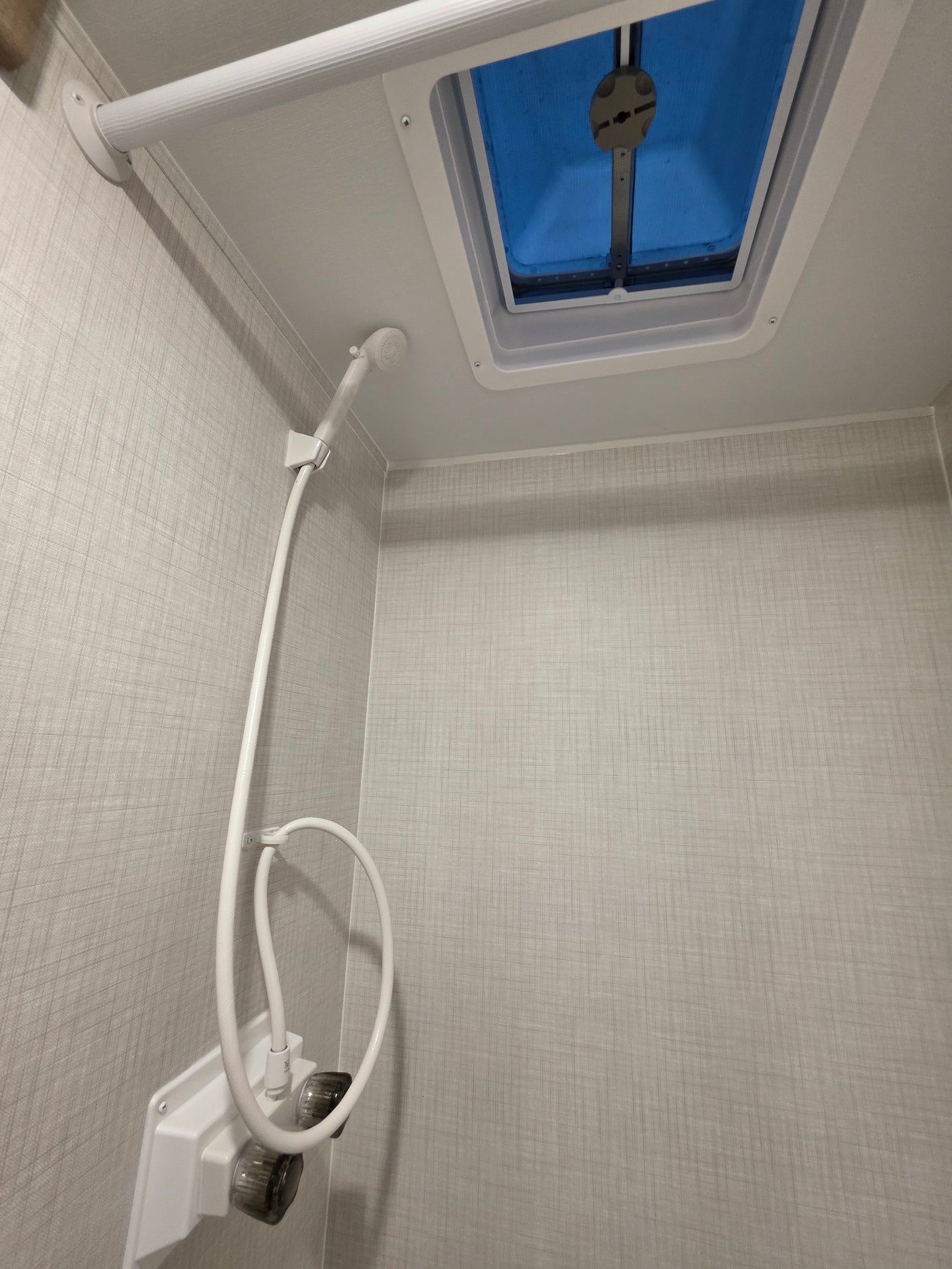 Inside an RV rental: a compact bathroom with a white shower head, water controls, and a blue-tinted ceiling skylight.