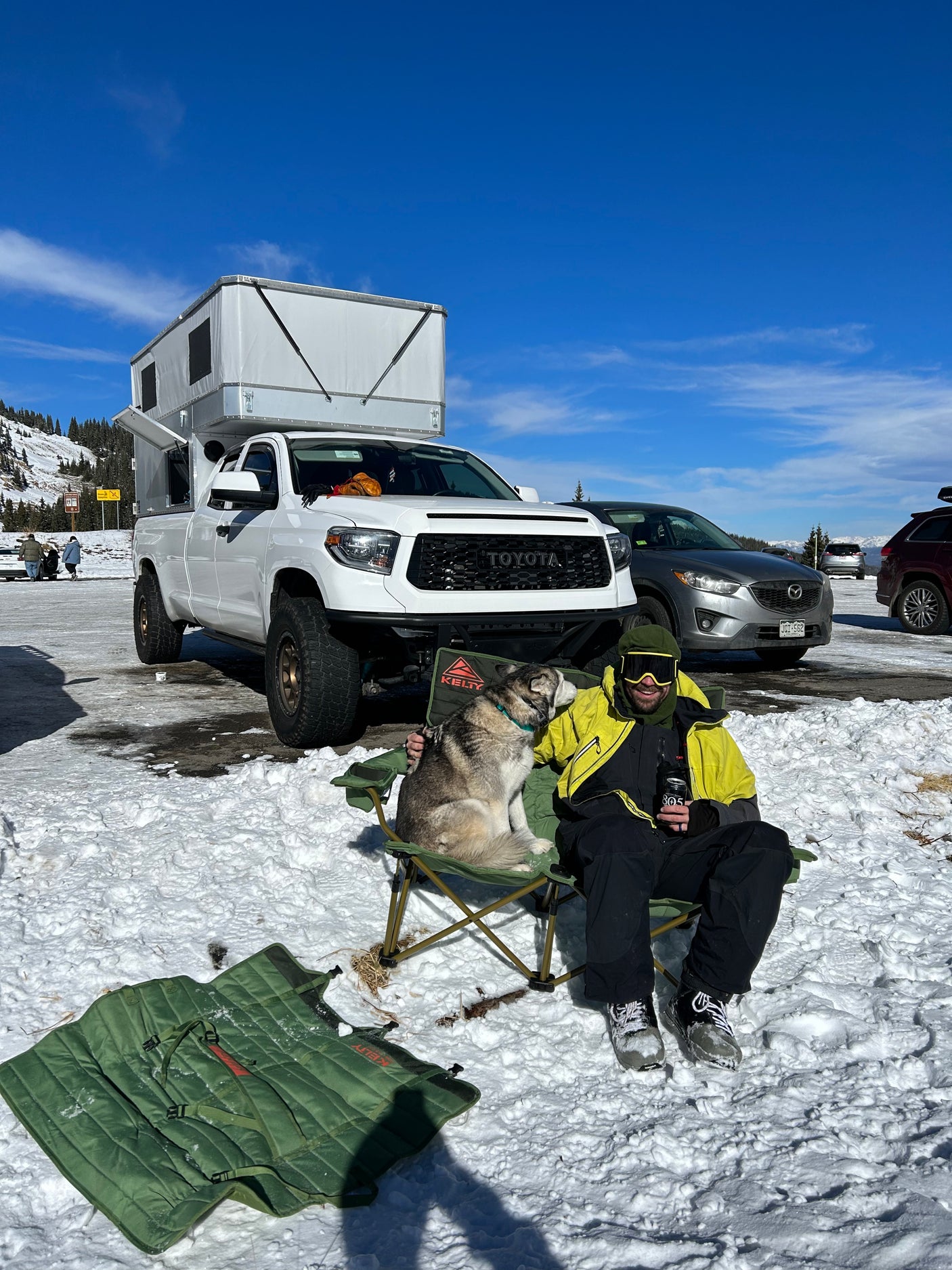 Man and dog relax in snow with a Toyota Tundra RV rental and pop-up camper. Great winter adventure.