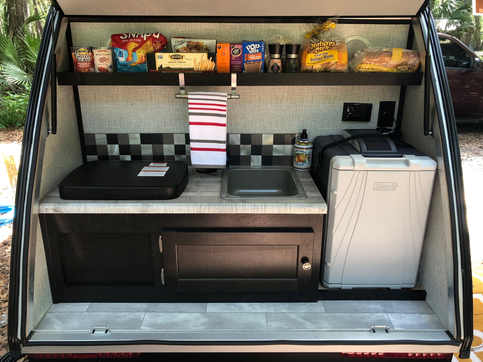 RV rental outdoor kitchen, well-stocked with food, cooktop, sink, and cooler, ready for camping.
