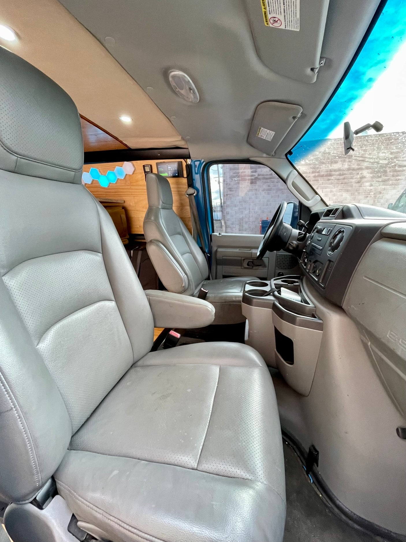 Interior of an RV rental van, showing gray front seats, dashboard, and custom-built wood paneling in the rear.