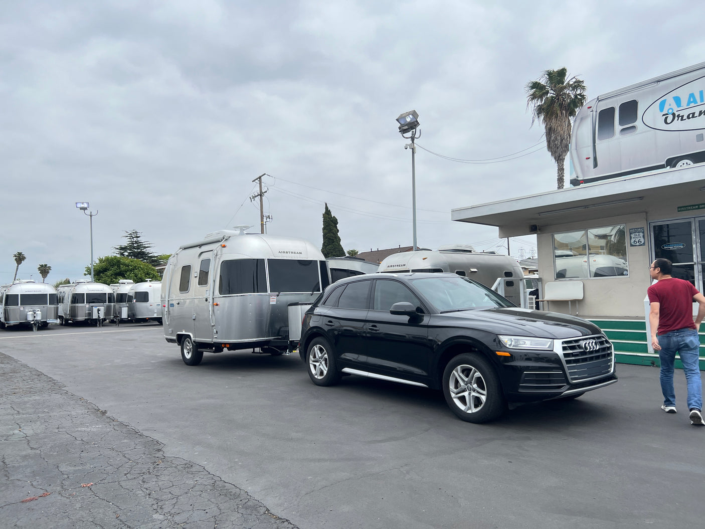 An Audi SUV is hitched to a silver Airstream travel trailer at an RV rental lot with more Airstreams visible.