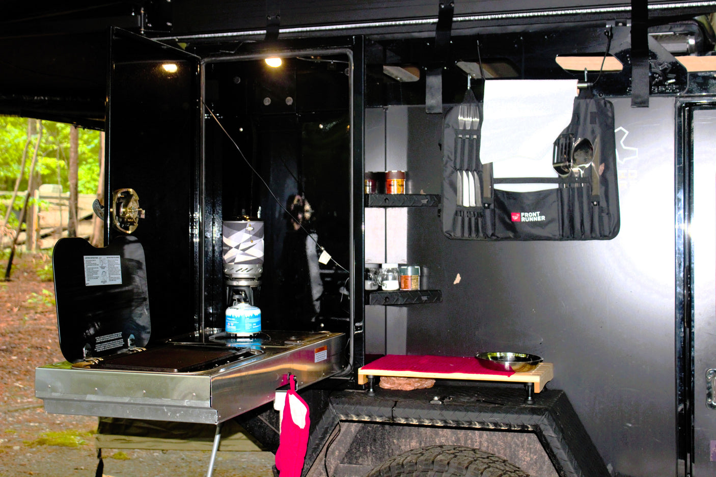 This RV rental features a well-equipped outdoor camp kitchen. Visible are a stove, utensils, spices, and a small prep area, ready for cooking.