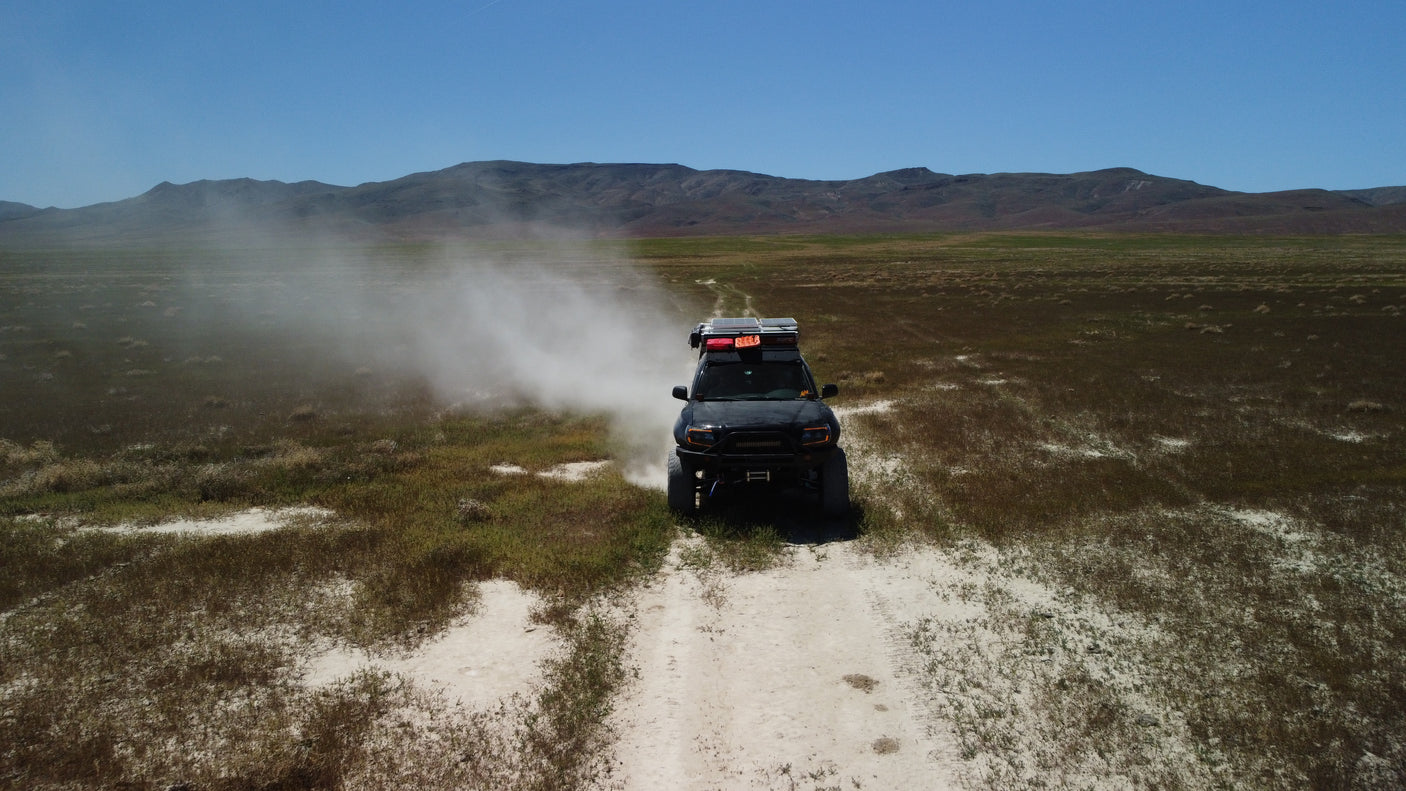 An overland vehicle creates a dust cloud while driving on a dirt trail through a vast, grassy plain. Explore with an RV rental!