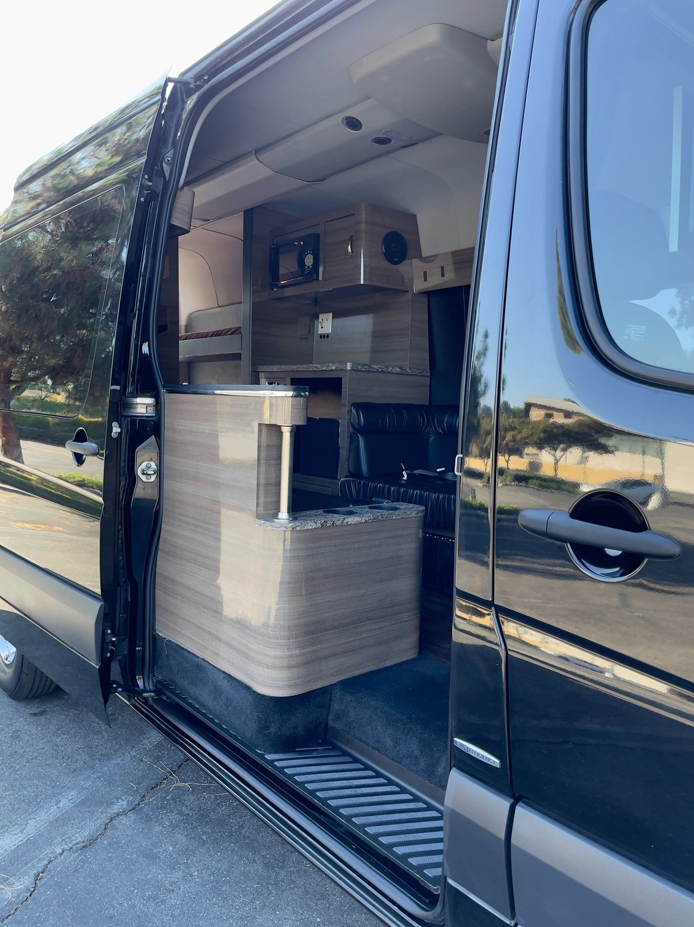 Open side door of a sleek black RV rental van, revealing a custom interior with compact kitchen and lounge area.