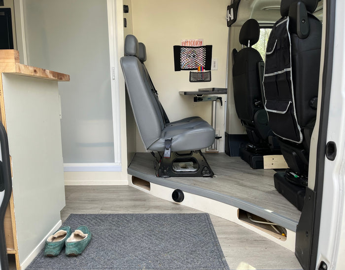 Cozy RV rental camper van interior with grey seating, wall-mounted table, unicorn art, and slippers.