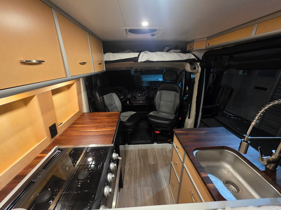 Spacious RV rental interior with a cozy bed, full kitchen, and modern wood cabinetry, perfect for your next adventure.