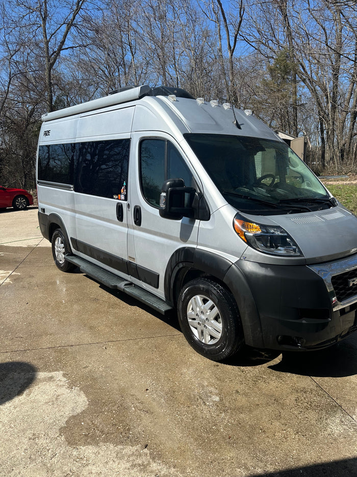 A sleek silver RV rental camper van parked on a sunny concrete driveway, hinting at outdoor travel and adventure.