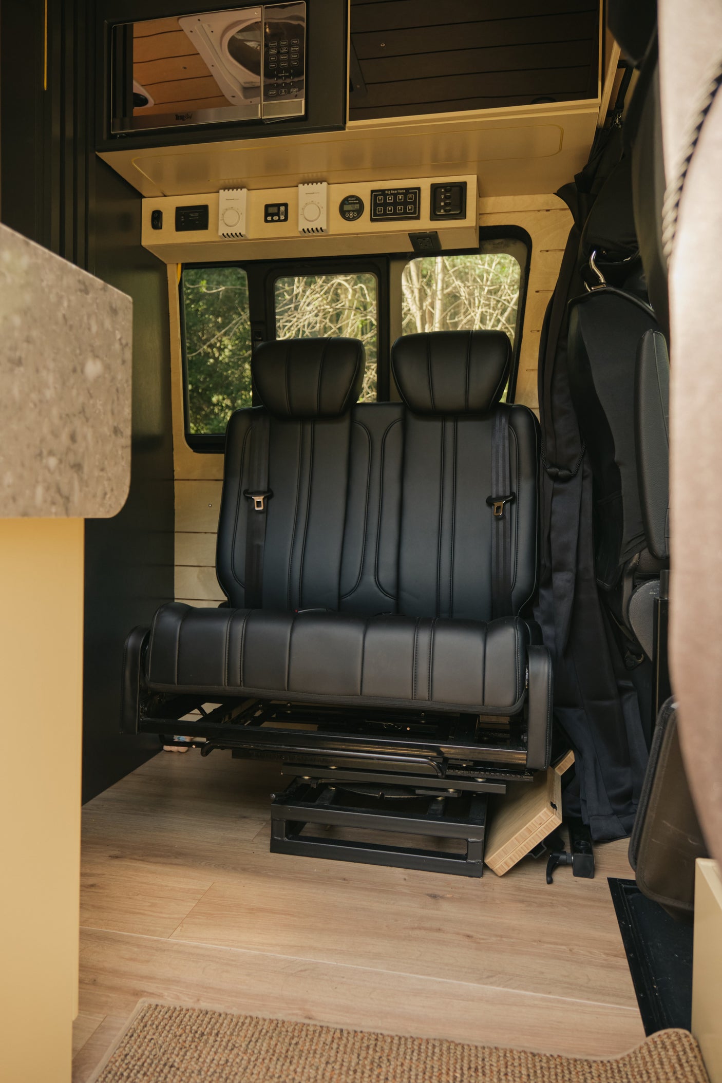 Inside an rv rental: black passenger seats, control panel, and microwave setup. Wood-accented, cozy travel space.