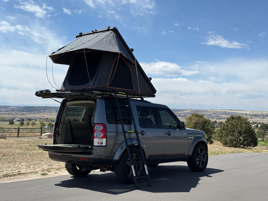 Grey Land Rover Discovery 4 SUV with an open rooftop tent & ladder, ready for your next rv rental adventure.