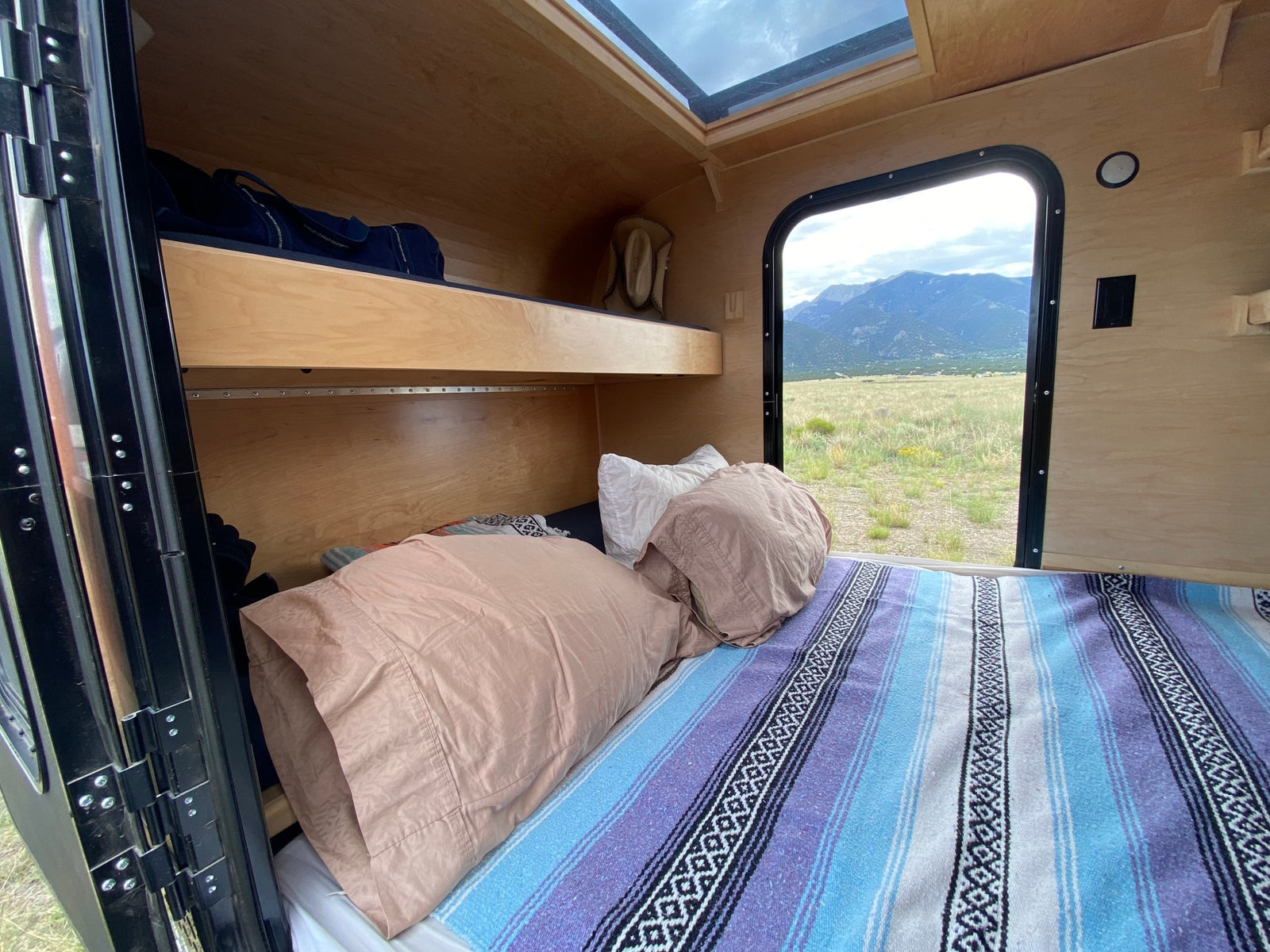 RV rental interior with a comfy bed, bunk, and skylight. Enjoy panoramic mountain views from the large window.