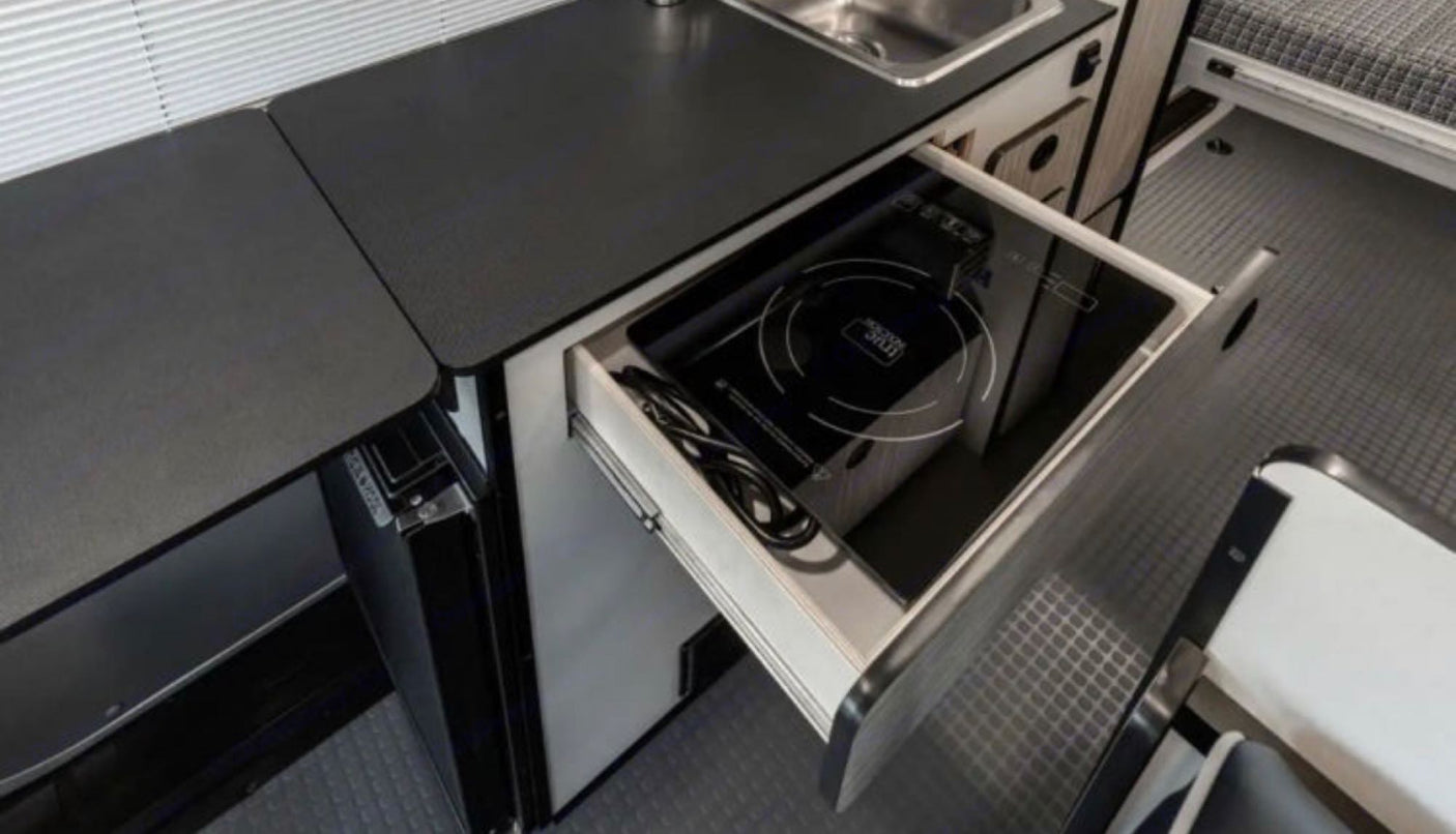 Smart RV rental kitchen design: A pull-out drawer reveals a portable induction cooktop next to the sink and fridge.