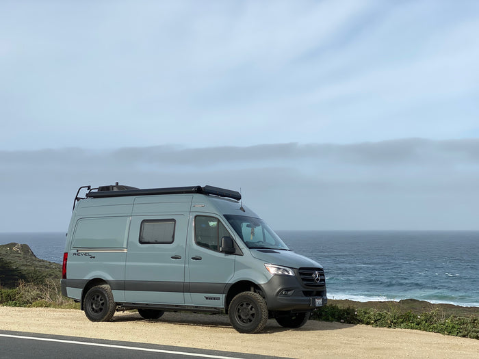 A grey Winnebago Revel 4x4 camper van by scenic ocean, great for an rv rental trip.