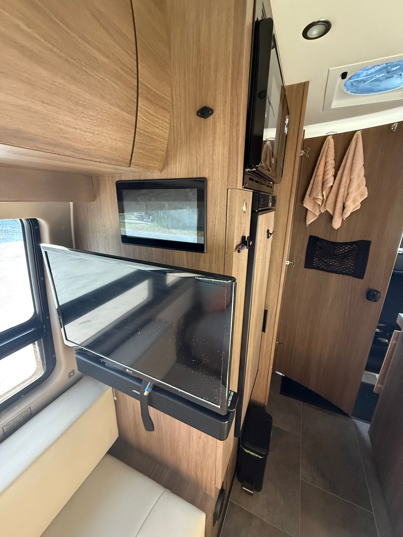 Inside a modern RV rental: wood interior, dual TVs, microwave, fridge, and cozy seating area.