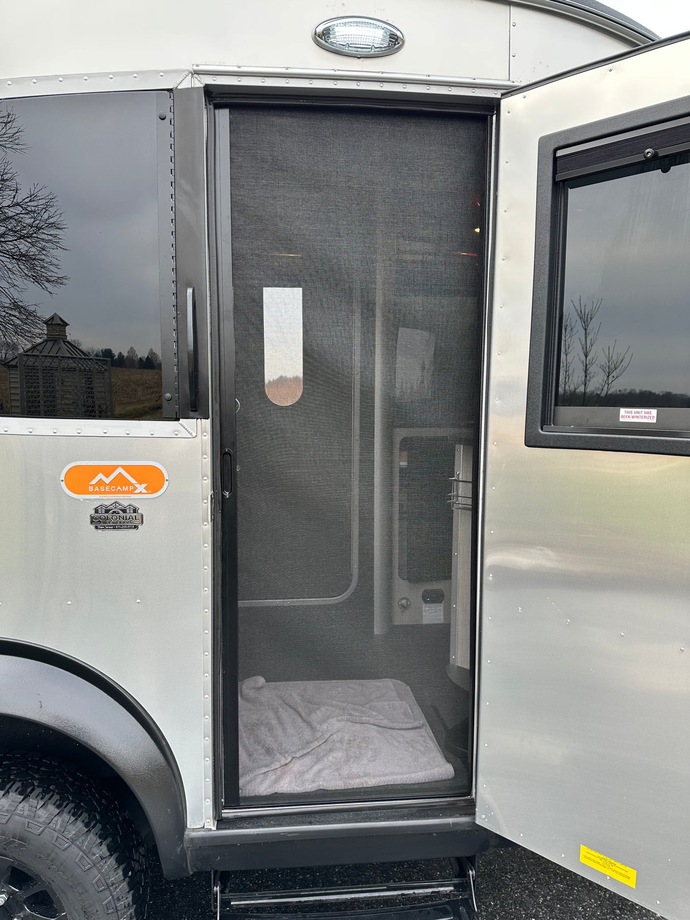 Inside an Airstream Basecamp RV rental with its screen door open, showing the interior and a "winterized" sticker.