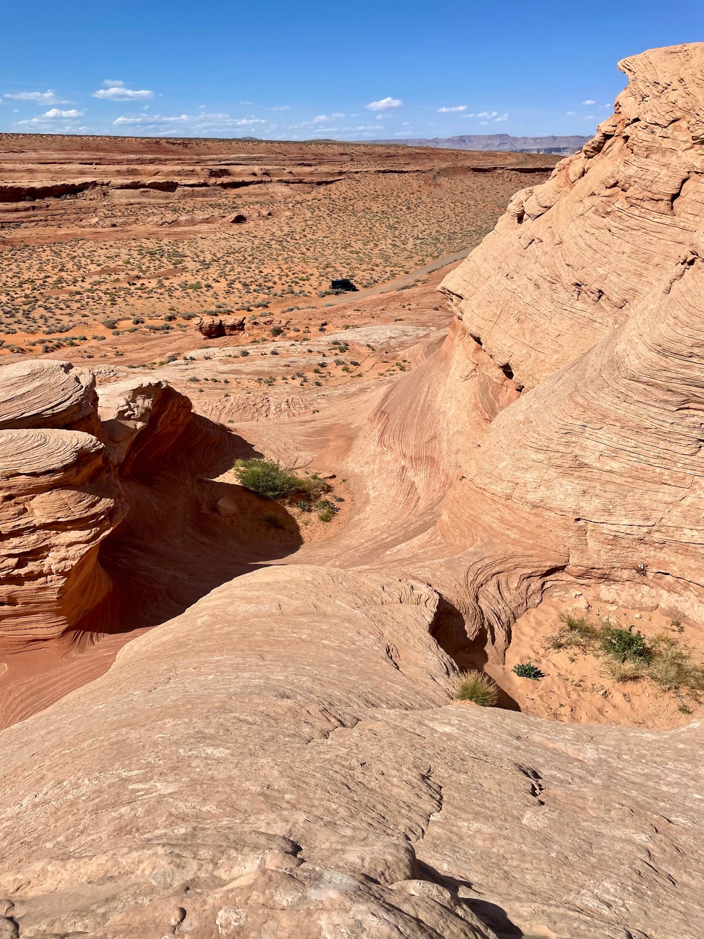 Spectacular desert landscape: deep, sculpted sandstone canyon overlooks plains with an RV rental on a distant track.