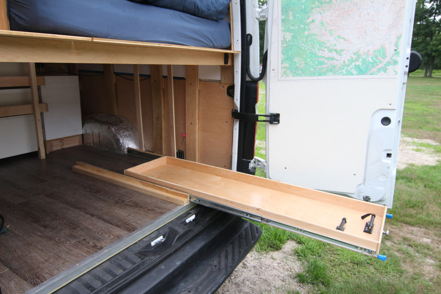 RV rental: Camper van conversion with extended pull-out storage tray, elevated bed, and wood flooring. Spacious interior.