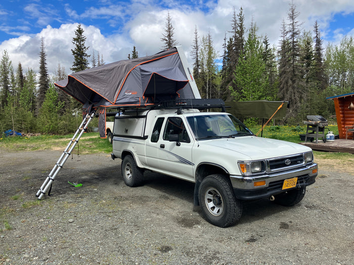 White pickup truck with a deployed rooftop tent, offering an RV rental alternative for camping and overlanding in Alaska.
