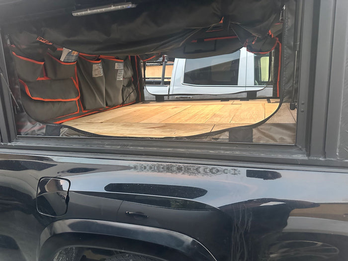 and front seats. Excellent for your next RV rental journey.|Modified black truck with rooftop tent & awning. An RV rental is visible by mountains & water in a gravel campground.|Optimized RV rental cargo space featuring wooden benches