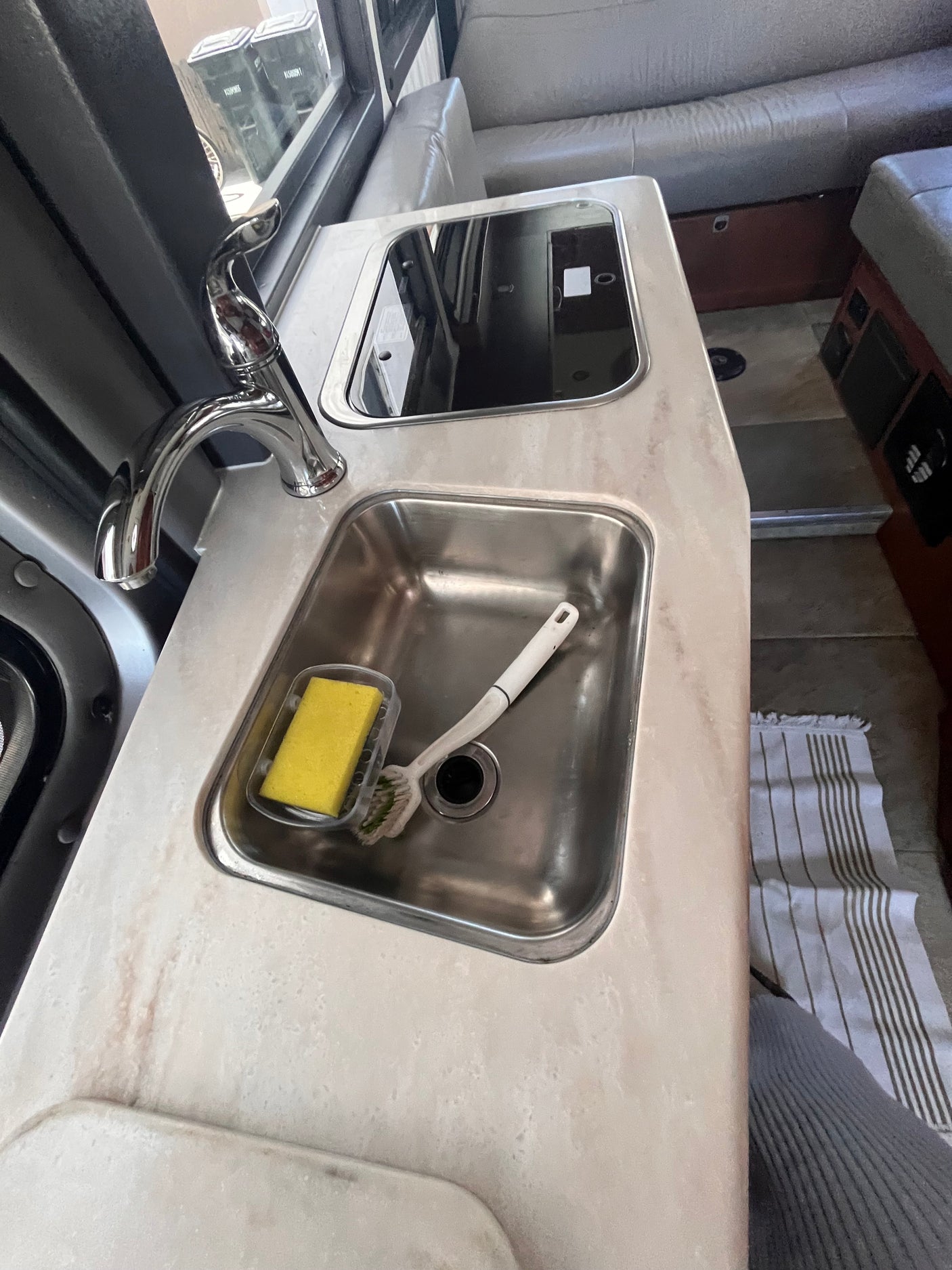 Inside an RV rental: Compact kitchenette with stainless steel sink, faucet, and cooktop. Featuring cozy sofa seating.