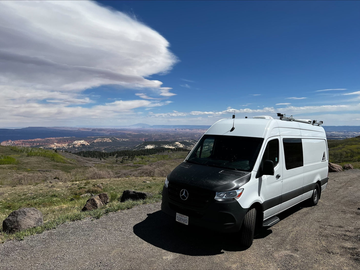 Our white Mercedes Sprinter camper van rv rental parked overlooking a vast mountain landscape under a blue sky.