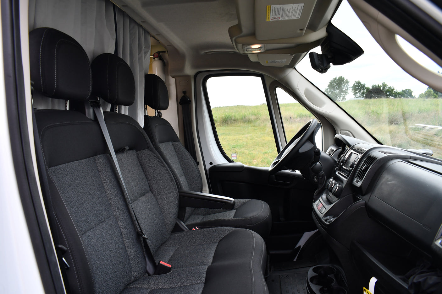 RV rental van's front cabin: driver & passenger seats, dashboard, and a clear view of a grassy field outside.