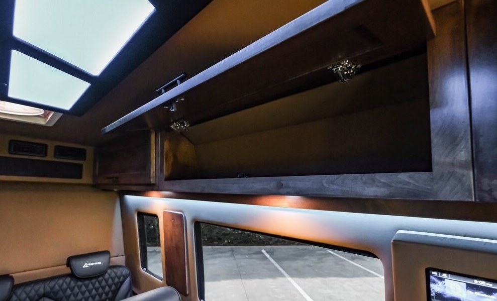 Interior of an RV rental: open overhead storage, skylights, ambient lighting, and large windows revealing the outside. — photo 16