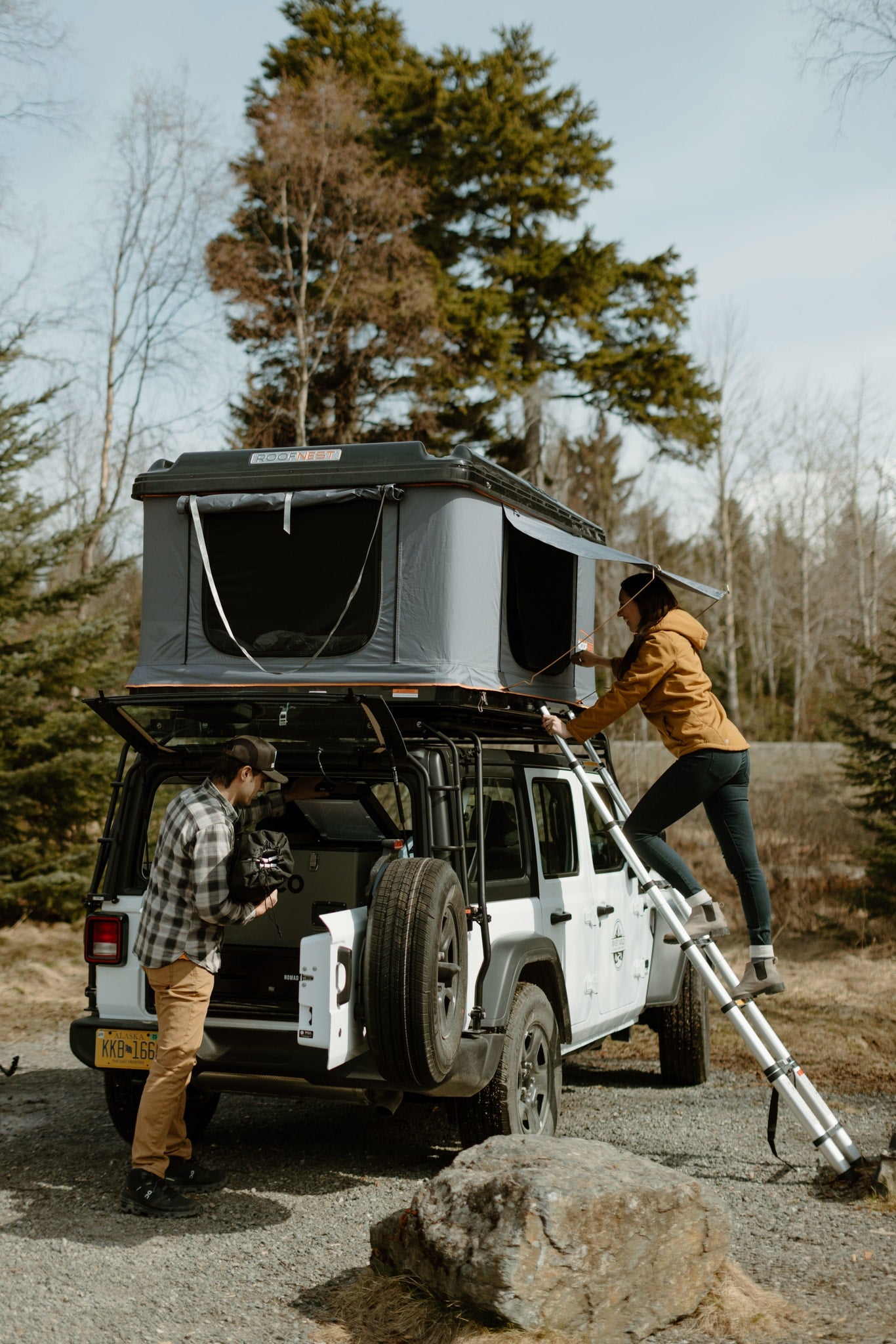 Two people set up a Roofnest rooftop tent on a white Jeep Wrangler. Perfect for an outdoor RV rental or camping adventure.