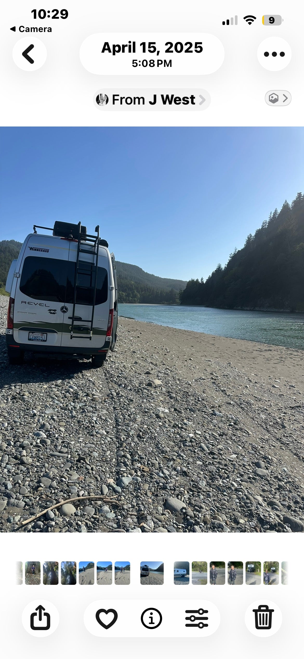 Scenic rv rental adventure: A white Winnebago Revel camper van parked on a rocky riverbank with forested hills and a calm river.