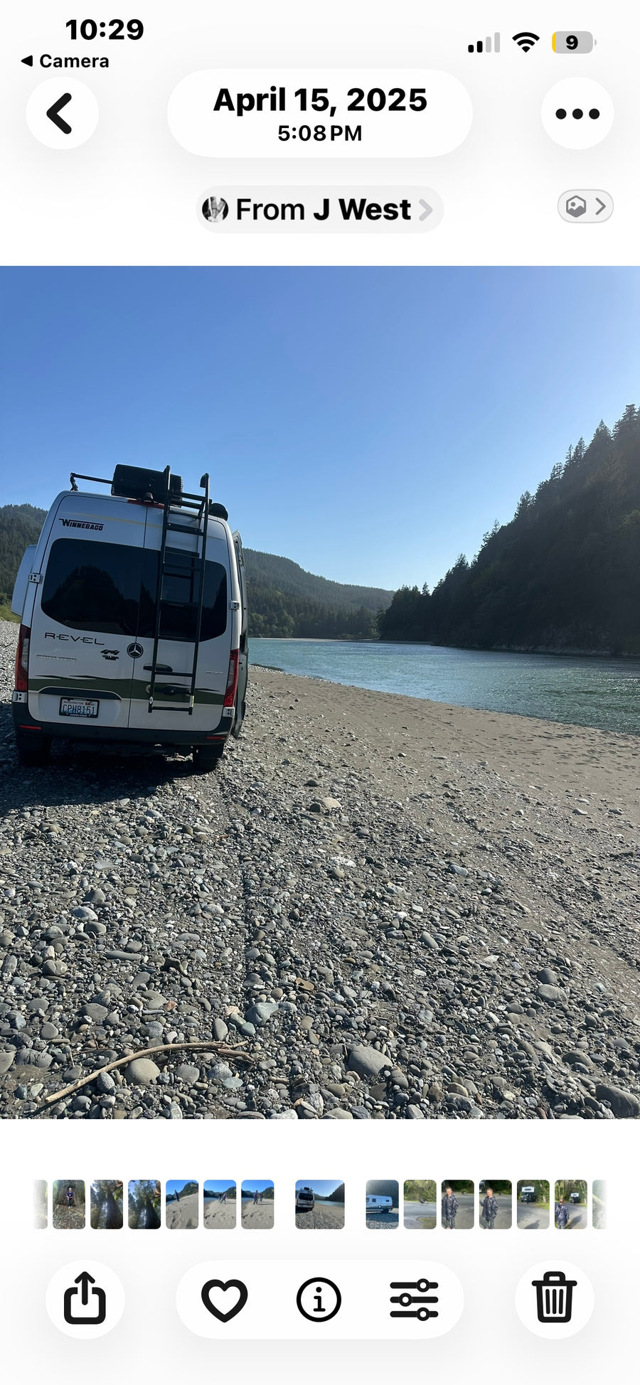 Scenic rv rental adventure: A white Winnebago Revel camper van parked on a rocky riverbank with forested hills and a calm river.