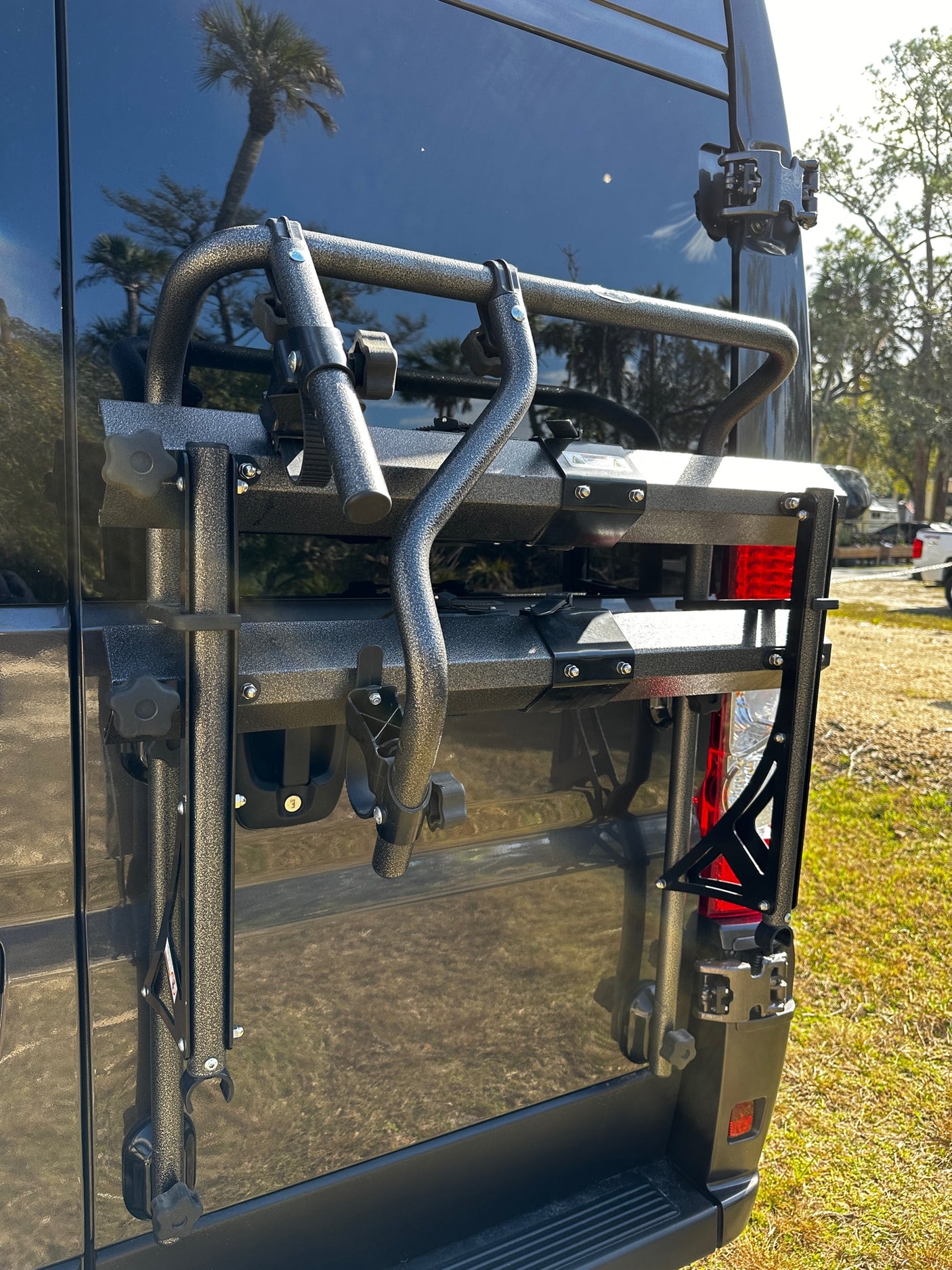 Durable, speckled gray rack on the back of an RV rental, designed for carrying outdoor gear. Palm tree visible in reflection.