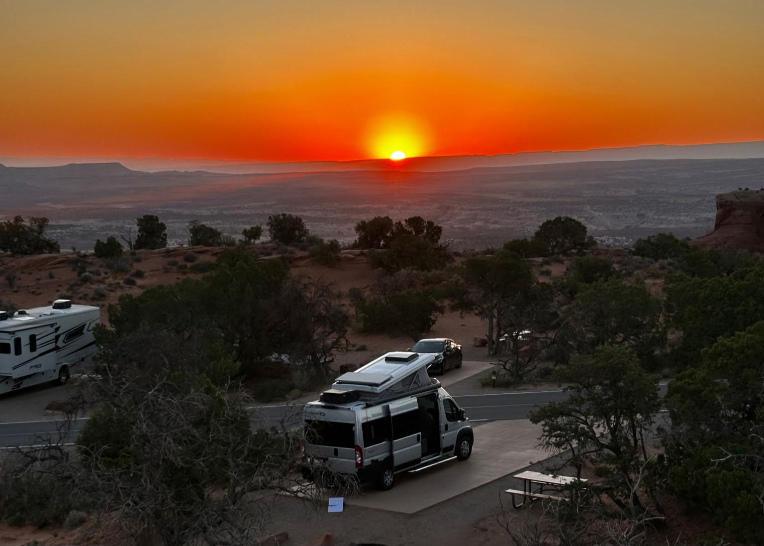 Experience adventure! An RV rental and another RV are parked at a desert campsite under a stunning sunset.