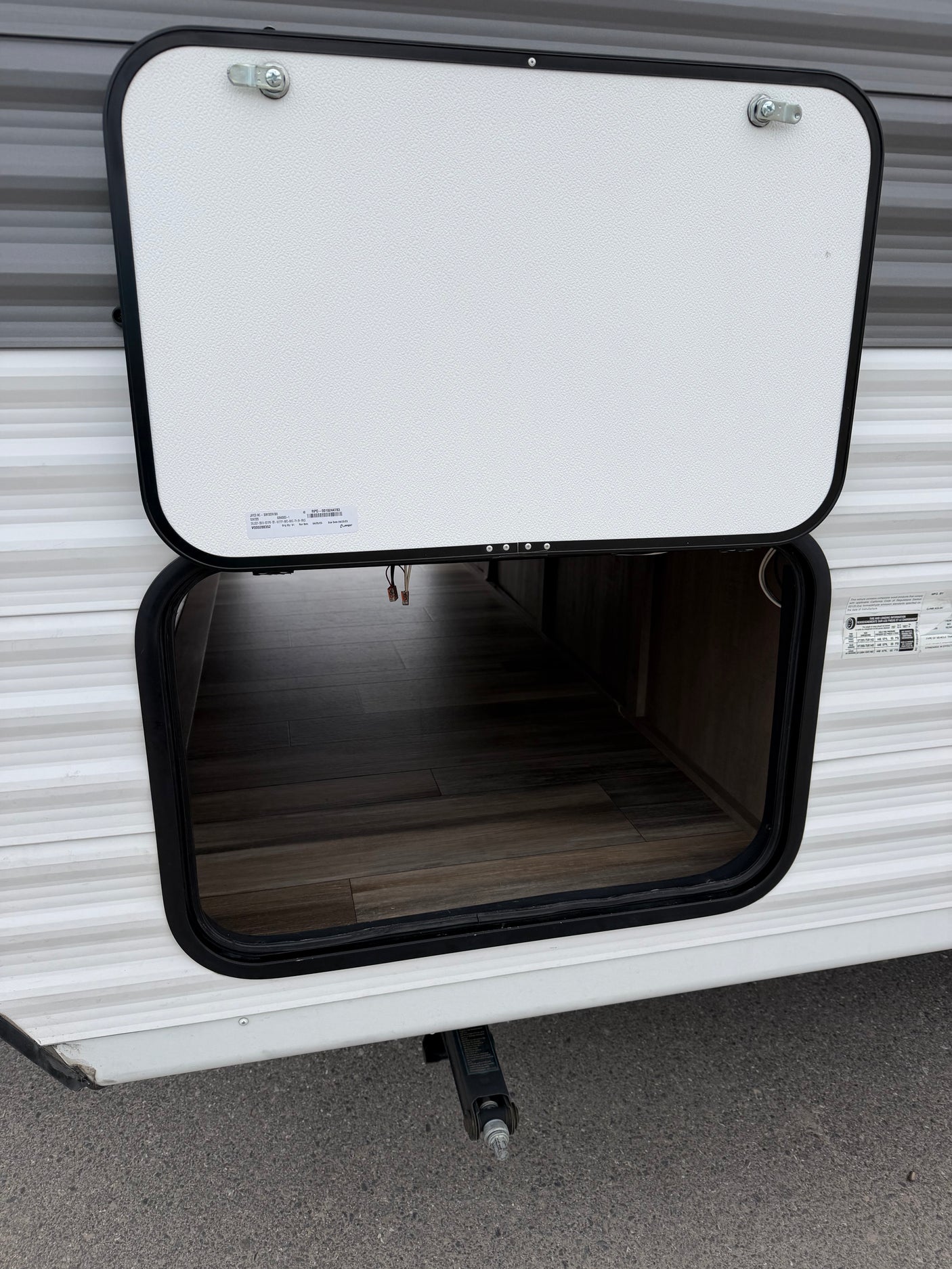 Open exterior storage compartment on an RV rental, revealing a wood-look floor. A leveling jack is seen below.